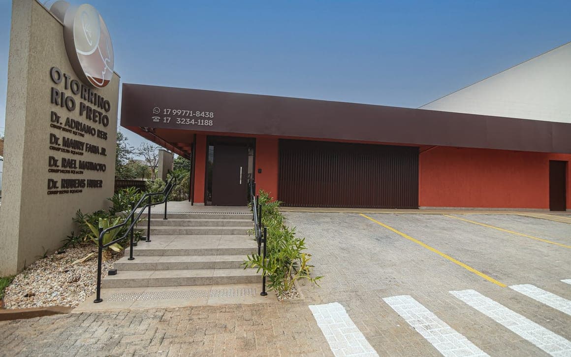 Fachada do consultório, com escada, corrimão e estacionamento à frente